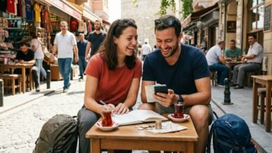 صورة واقعية لزوجين سائحين في إسطنبول، تركيا، يضحكان أثناء تخطيط ميزانية رحلتهما وحساب التكاليف في مقهى شعبي. تظهر على الطاولة عملات ليرة تركية ودفتر ملاحظات، وفي الخلفية برج غلطة وأجواء السوق المزدحمة