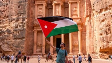 سائح يحمل العلم الأردني بفخر أمام مبنى الخزنة الشهير في مدينة البتراء الأثرية، الوجهة الرئيسية التي تغطيها التذكرة الموحدة (Jordan Pass).