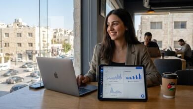 رائدة أعمال أردنية تحلل بيانات التسويق عبر منصات التواصل والمبيعات بالدينار الأردني على لوحة تحكم رقمية في جلسة على سطح بعمان لعام 2026.